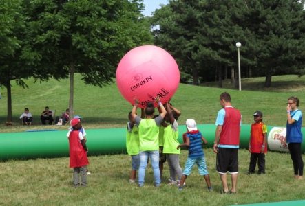Shev123 Un groupe d'enfant en train de jouer avec un ballon rose gigantesque, tenu au-dessus de leurs têtes.