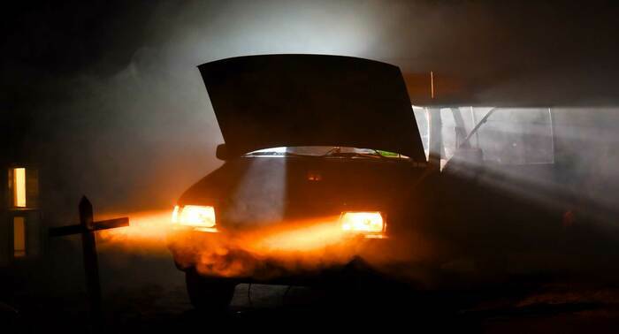 Une voiture avec une porte et le capot ouvert ainsi que les feux allumés dans l'obscurité.