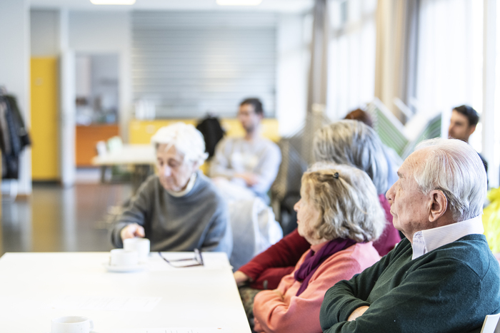 Trois seniors sont assis autour d'une table, on les voit de profil et ils regardent en direction d'une personne qui n'apparaît pas sur l'image