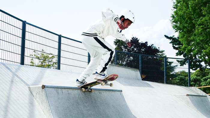 Un jeune skateur en tenue blanche effectue une figure sur une rampe en béton dans un skatepark.