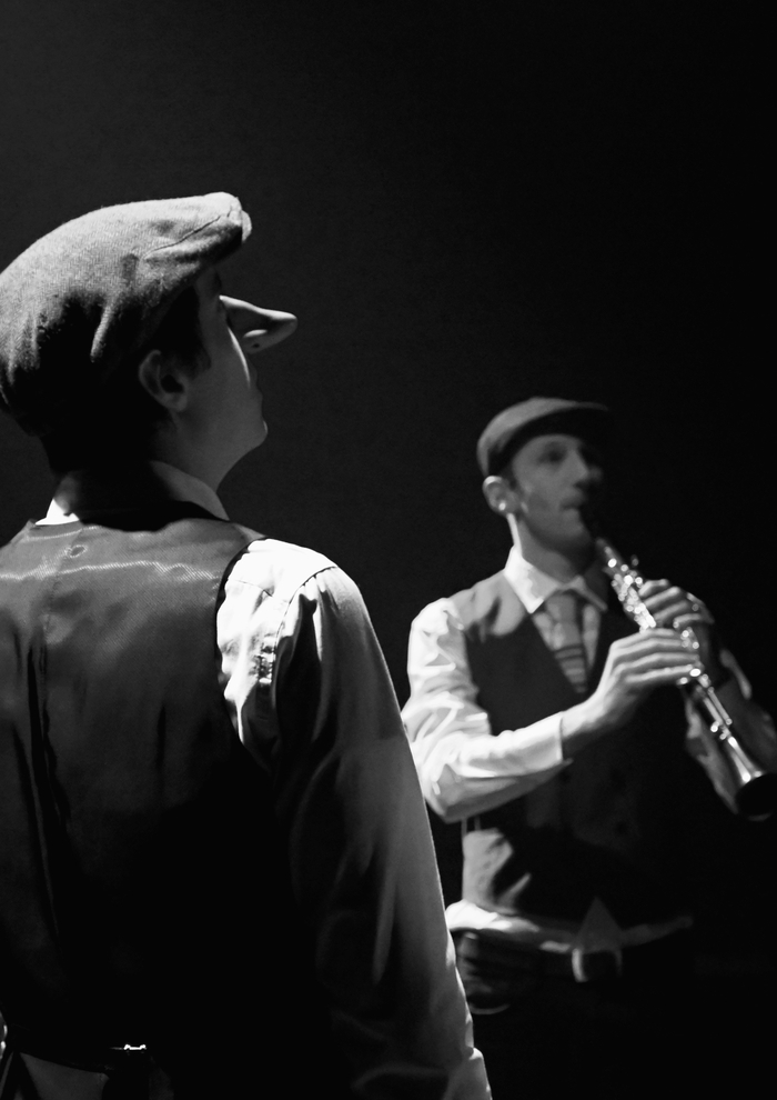 Photo d'un comédien debout avec un long nez et un autre jouant de la flute