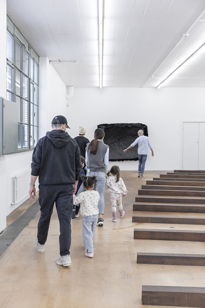 Parents et enfants marchant à côté d'une oeuvre Richard Nonas au MAMCO