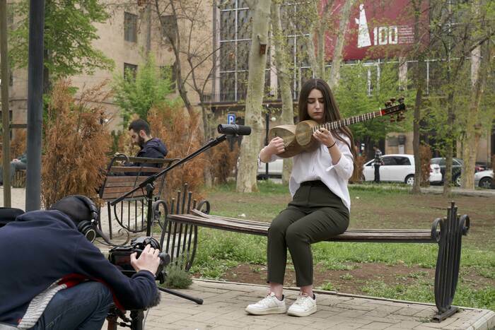 Arthur Henry filmant une jeune femme assise sur un banc jouant du "tar".