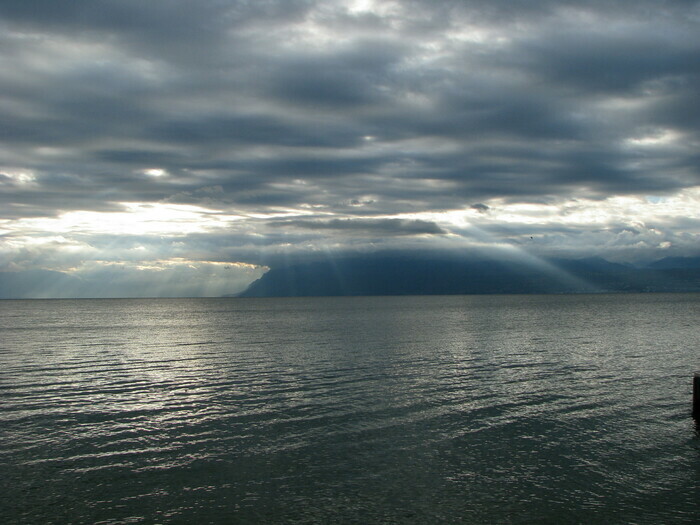 Photo du Léman sous un ciel couvert à travers lequel les rayons du soleil passent.