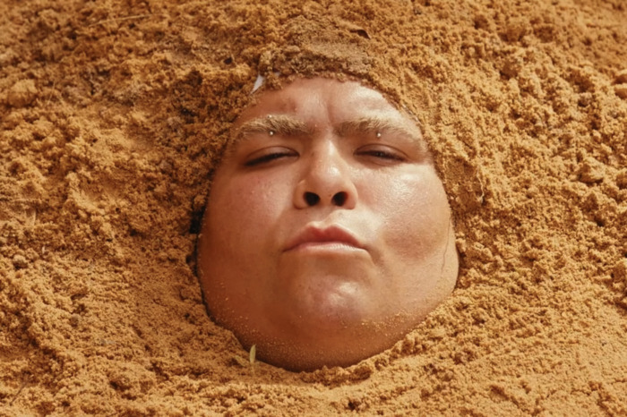 Portrait de l'artiste dont la tête est immergée dans du sable