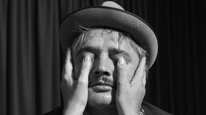 Portrait en noir et blanc de Peter Doherty les yeux fermés et des mains sur son visage