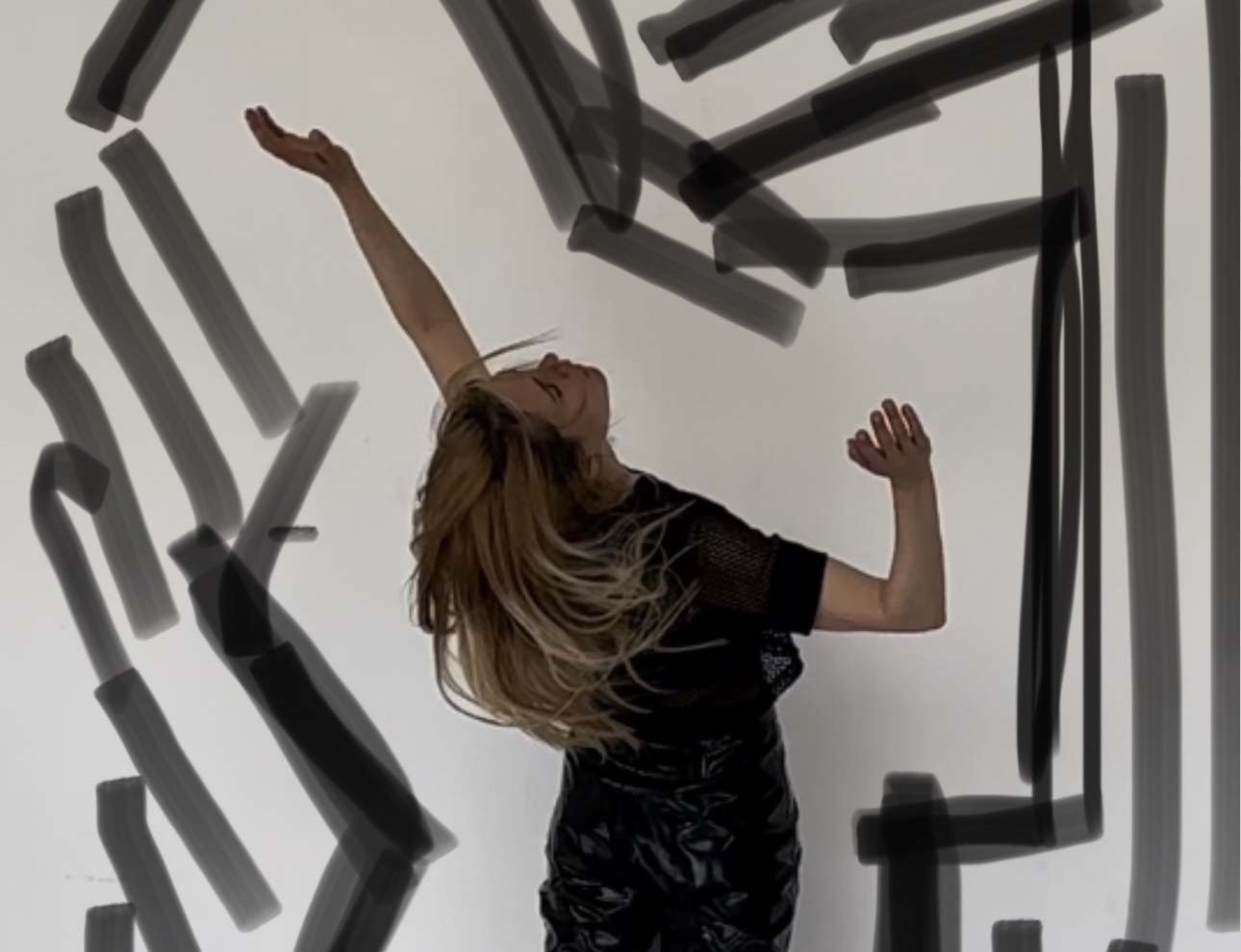 La danseuse Marie-Caroline Hominal est debout sur la pointe des pieds devant un mur blanc. Son corps penche en arrière. Elle est habillée d'un pantalon et d'un t-shirt noirs. Des traits dessinés entourent la silhouette de la danseuse.