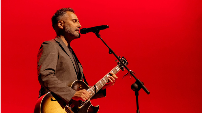 Photo de Joge Drexler jouant de la guitare et chantant dans un micros