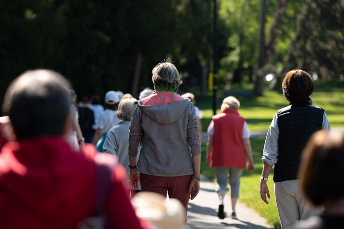 Des seniors vus de dos se baladent dans un parc.