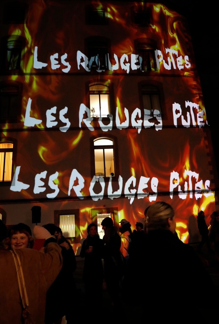 Projection du texte "Les Rouges Putes" sur une façade avec des illustrations de flammes