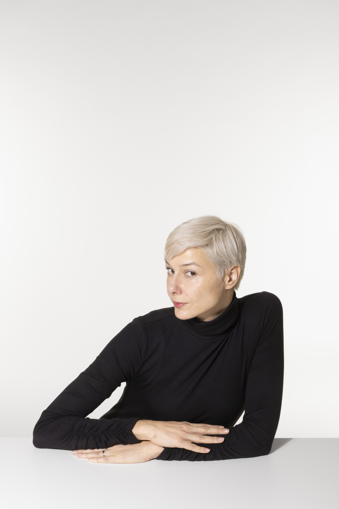 Une femme blanches aux cheveux courts avec un pull noir pose devant la caméra. C'est l'écrivaine Ed Wige.