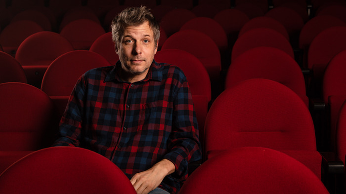 Nathanaël Rochat assis sur des chaises de théâtre rouge