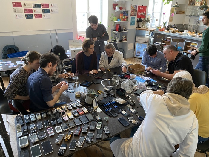 Atelier démontage de smartphone, avec une dizaine de personnes autour de tables où sont étalés plusieurs dizaines de téléphones