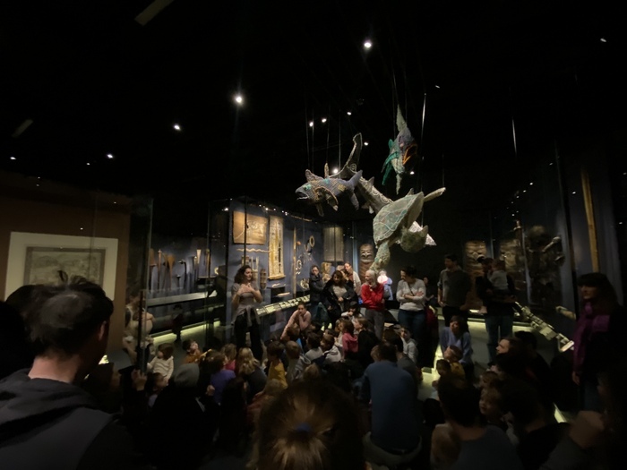 Un groupes d'enfant et d'adultes devant une animatrice dans l'exposition permanente du MEG à Genève.