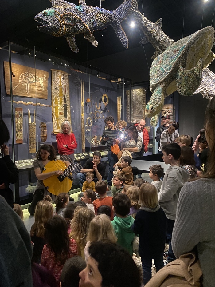 Un groupes d'enfant et d'adultes devant une animatrice dans l'exposition permanente du MEG à Genève.