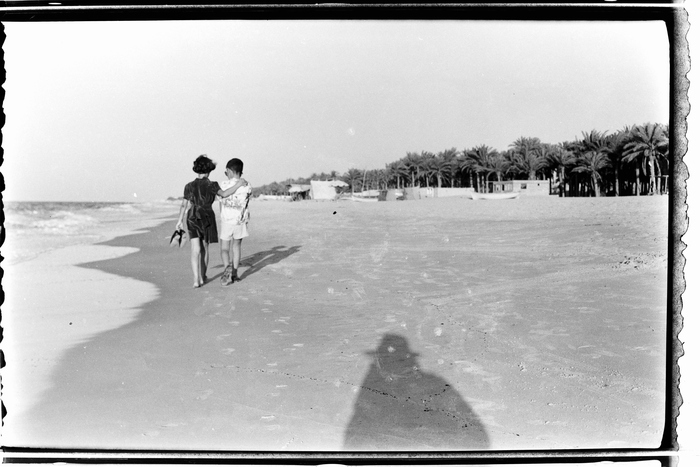 Une photo en noir et blanc avec deux petites filles marchant sur la plage. En bas, à droite de l'image, on voit l'ombre du photographe sur le sable.