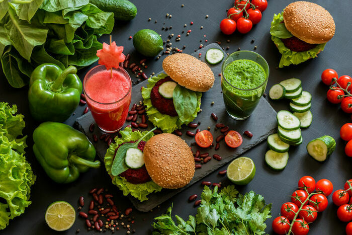 Une photo en couleur qui représente des poivrons, des tomates, des jus de légumes vert et rose et des sandwiches