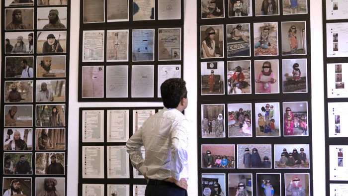 Un homme observe un mur d'exposition rempli de photos, de documents et de témoignages sur les survivant·es yézidi·es, mettant en lumière les horreurs subies et la quête de justice et de réparation.