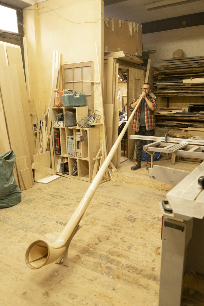 Sandro Faïta dans son atelier en train de jouer du cor des Alpes