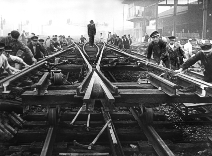 Travailleurs posant des rails de chemin de fer sous une atmosphère brumeuse, illustrant l'effort collectif et l'industrialisation en noir et blanc.