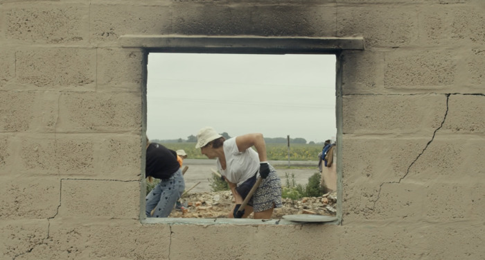 Des personnes déblayant des débris à travers la fenêtre d'un bâtiment en ruines, illustrant la résilience et la reconstruction en Ukraine.