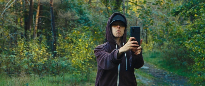 Une personne en sweat à capuche et casquette prenant un selfie en pleine forêt.