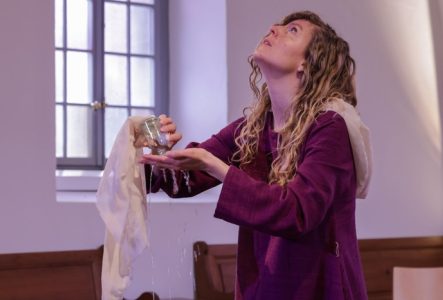 Une femme lève les yeux au plafond en versant le liquide contenu dans une fiole sur sa main. Elle est dans une église.