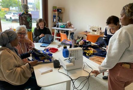 Sur cette photo, on aperçoit l'atelier de customisation de vêtements et accessoires. Cinq participants, aux origines et âges variés, travaillent autour d'une grande table, entourés de tissus, fils et outils. Ángela, l'animatrice, les guide dans la réparation et la création des vêtements qu'ils ont apportés. Chacun se concentre sur sa tâche : certains recousent, d'autres ajoutent des décorations ou ajustent des détails. L'ambiance est chaleureuse et collaborative, où l'échange entre cultures et…