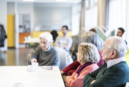 Trois seniors sont assis autour d'une table, on les voit de profil et ils regardent en direction d'une personne qui n'apparaît pas sur l'image