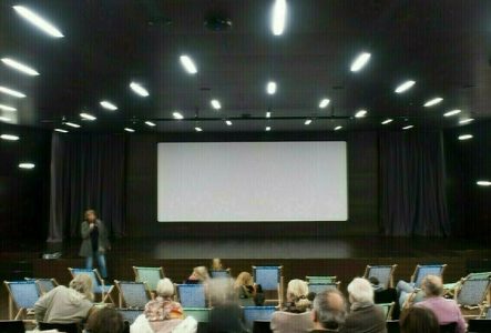 Une salle de projection avec des spectateurs et spectatrices vues de dos