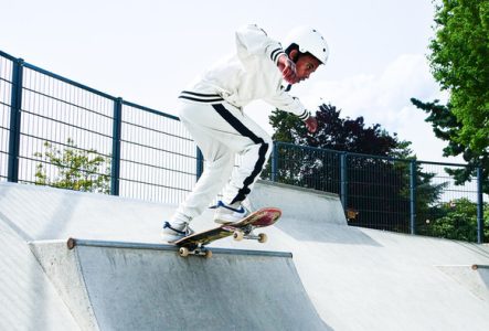 Un jeune skateur en tenue blanche effectue une figure sur une rampe en béton dans un skatepark.