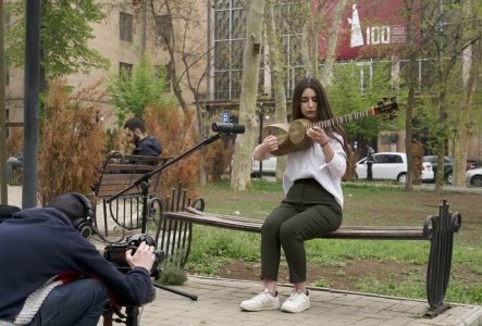 Arthur Henry filmant une jeune femme assise sur un banc jouant du "tar".