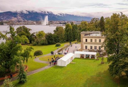 Des tentes de festival avec des gens devant le Musée d'Histoire des Sciences de la ville de Genève, au bord du lac Léman.