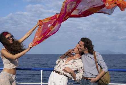 Trois jeunes gens jouent avec un foulard sur un bateau en Méditerranée.