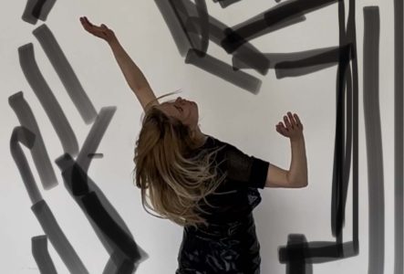 La danseuse Marie-Caroline Hominal est debout sur la pointe des pieds devant un mur blanc. Son corps penche en arrière. Elle est habillée d'un pantalon et d'un t-shirt noirs. Des traits dessinés entourent la silhouette de la danseuse.