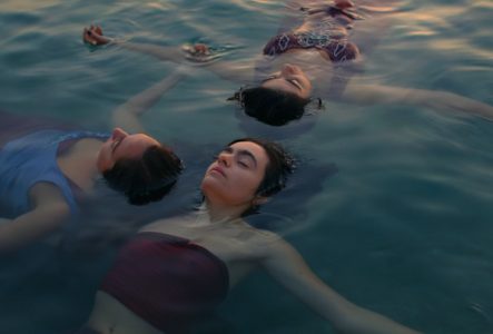 Trois femmes flottant paisiblement à la surface de l'eau, les yeux fermés, exprimant la sérénité, la résilience et l'abandon en pleine nature.