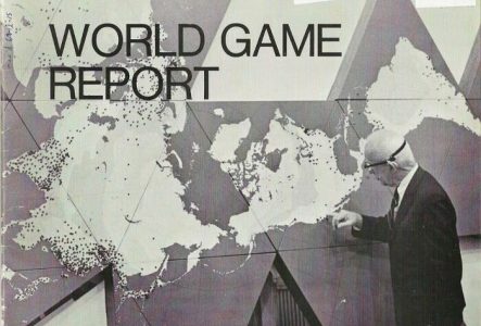 Sur cette image en noir et blanc on voit un homme en costume qui touche du doigt une carte du monde qui a été dessinée sur des triangles placés au mur. L'homme semble âgé. La carte du monde est difficilement reconnaissable. Les mots WORLD GAME REPORT sont inscrits en grand sur la partie supérieure gauche de l'image.