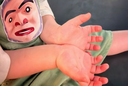 Les paumes des mains d'un enfant qui a un autocollant collé sur son habit. cet autocollant représente le masque d'un prince.