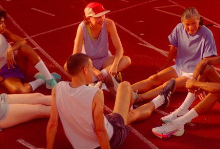 Groupe diversifié de personnes assises en cercle sur une piste d'athlétisme rouge, partageant un moment de convivialité et de complicité après une séance de sport.