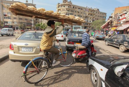 homme portant un plateau sur sa tête avec du pain, sur un vélo dans les rues du Caire, en Egypte - Claude Marthaler