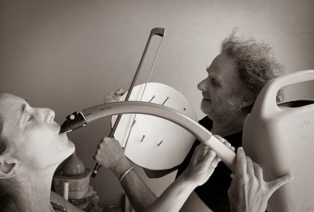 Un photo avec une musicienne au premier plan, en train de jouer avec un "arrosoir saxophone"