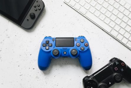 Une manette bleue posée entre des manettes noires, Switch et un clavier