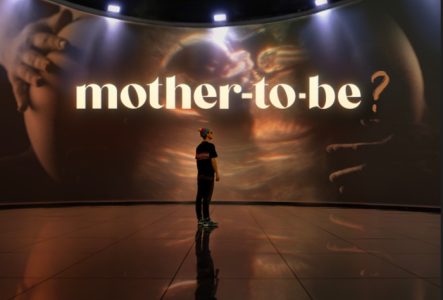 L'artiste Cee Roo se tient debout dans le Syllepse, une structure ronde et immersive à 360°. Il regarde la projection sur le thème de la maternité. On peut voir le ventre rond d'une femme et une échographie.