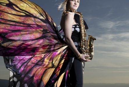 Valentine Michaud tenant son saxophone au bord du lac habillée d’une robe qui fait l’effet d’ailes de papillon dans le dos