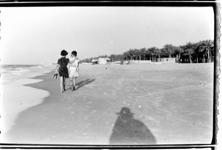 Une photo en noir et blanc avec deux petites filles marchant sur la plage. En bas, à droite de l'image, on voit l'ombre du photographe sur le sable.