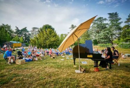 Un piano à queue et du public aui écoute assis dans l'herbe