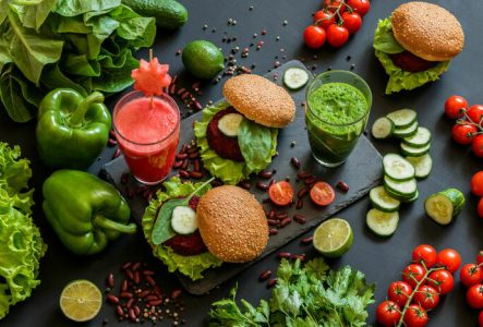 Une photo en couleur qui représente des poivrons, des tomates, des jus de légumes vert et rose et des sandwiches