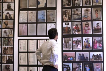 Un homme observe un mur d'exposition rempli de photos, de documents et de témoignages sur les survivant·es yézidi·es, mettant en lumière les horreurs subies et la quête de justice et de réparation.