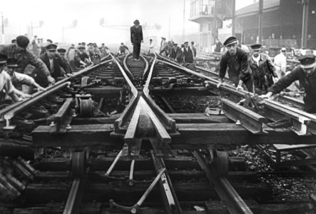 Travailleurs posant des rails de chemin de fer sous une atmosphère brumeuse, illustrant l'effort collectif et l'industrialisation en noir et blanc.