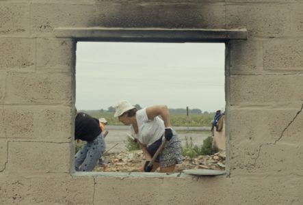 Des personnes déblayant des débris à travers la fenêtre d'un bâtiment en ruines, illustrant la résilience et la reconstruction en Ukraine.